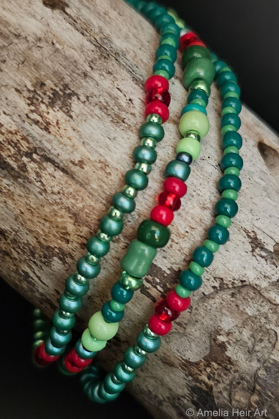 Three beaded bracelets in green, red, and light green on a wooden surface.