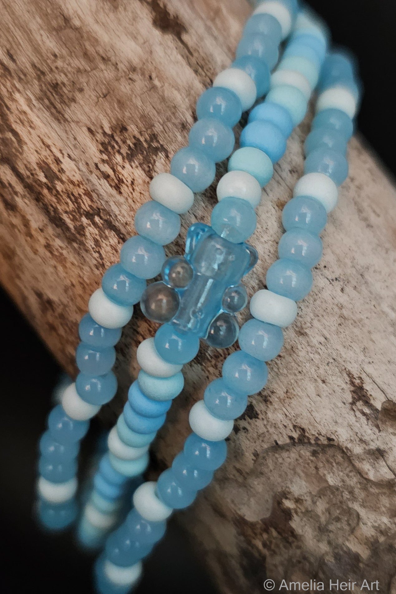 Three blue and white beaded bracelets with a gummy-bear-shaped bead on a wooden surface