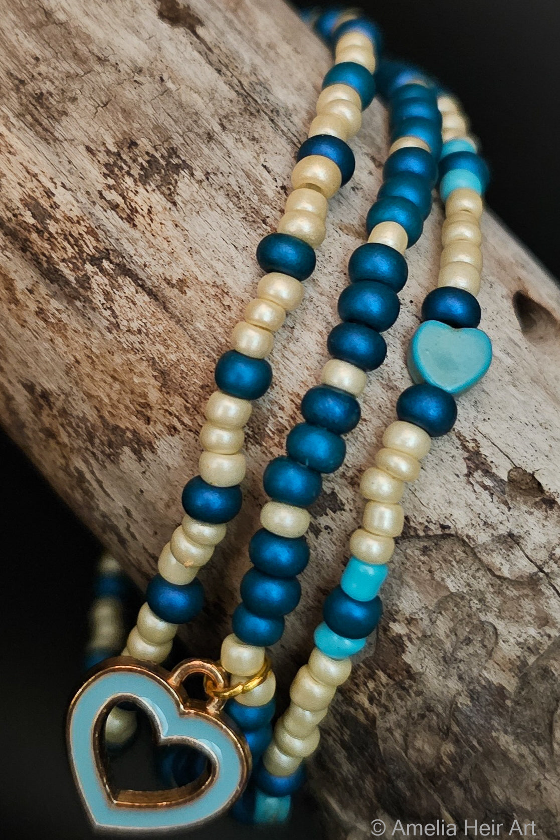 Three blue and cream beaded bracelets with a heart charm on a wooden surface