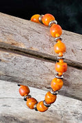 Bracelet with orange beads and silver accents on a wooden surface