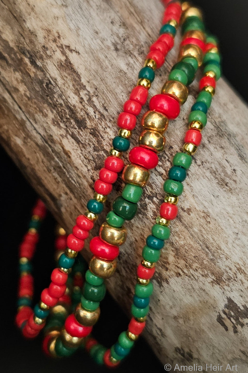 Three beaded bracelets in red, green, and gold on a wooden surface.