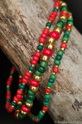 Three beaded bracelets in red, green, and gold on a wooden surface.