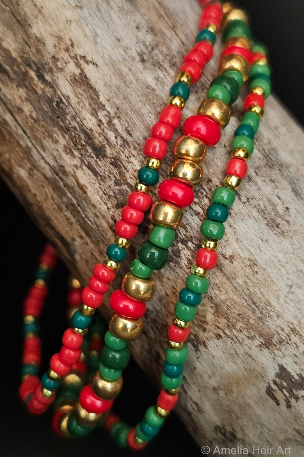 Three beaded bracelets in red, green, and gold on a wooden surface.