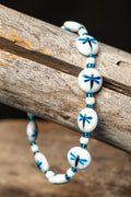 Bracelet with white beads and blue dragonfly designs on a wooden surface