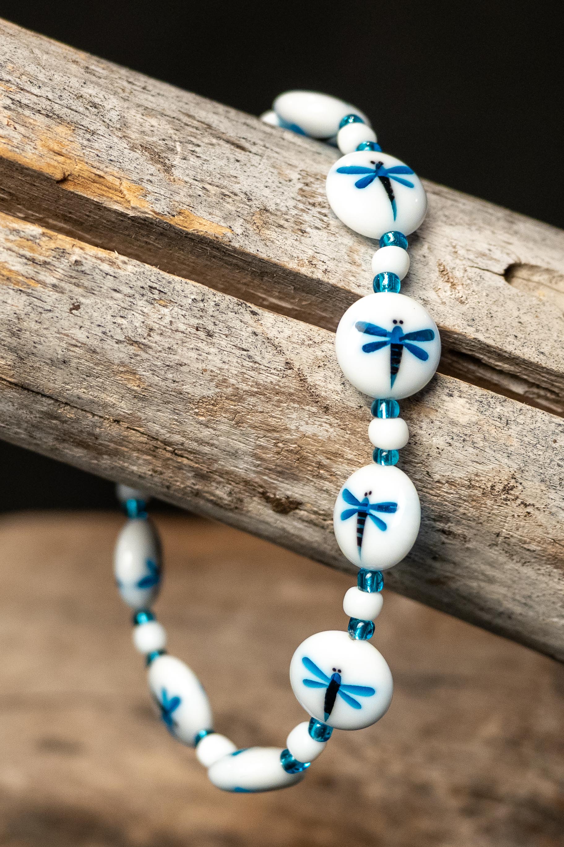 Bracelet with white beads and blue dragonfly designs on a wooden surface