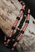 Three beaded bracelets with black and pink beads on a wooden surface.