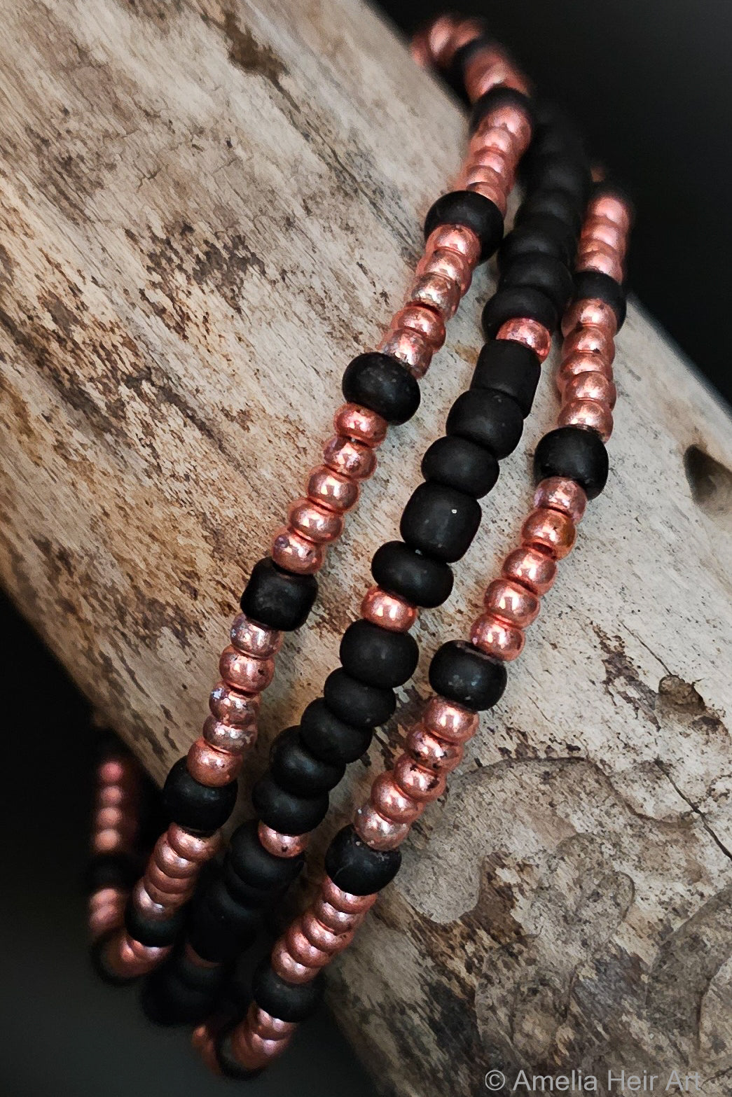 Three beaded bracelets with black and pink beads on a wooden surface.