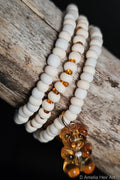 White beaded bracelet with amber beads and a bear charm on a wooden surface.