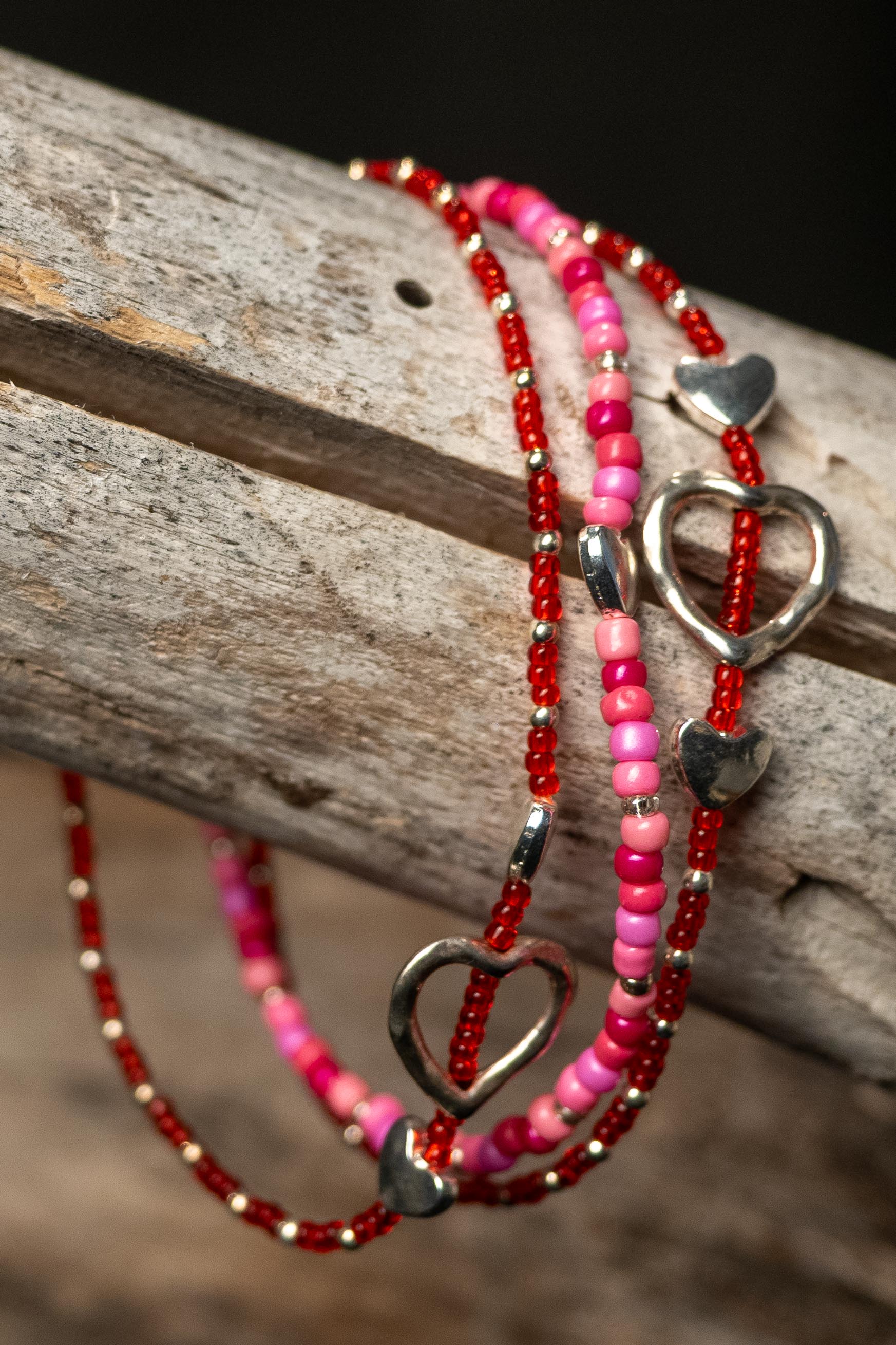 Three pink and red beaded bracelets with silver heart accents on a wooden surface