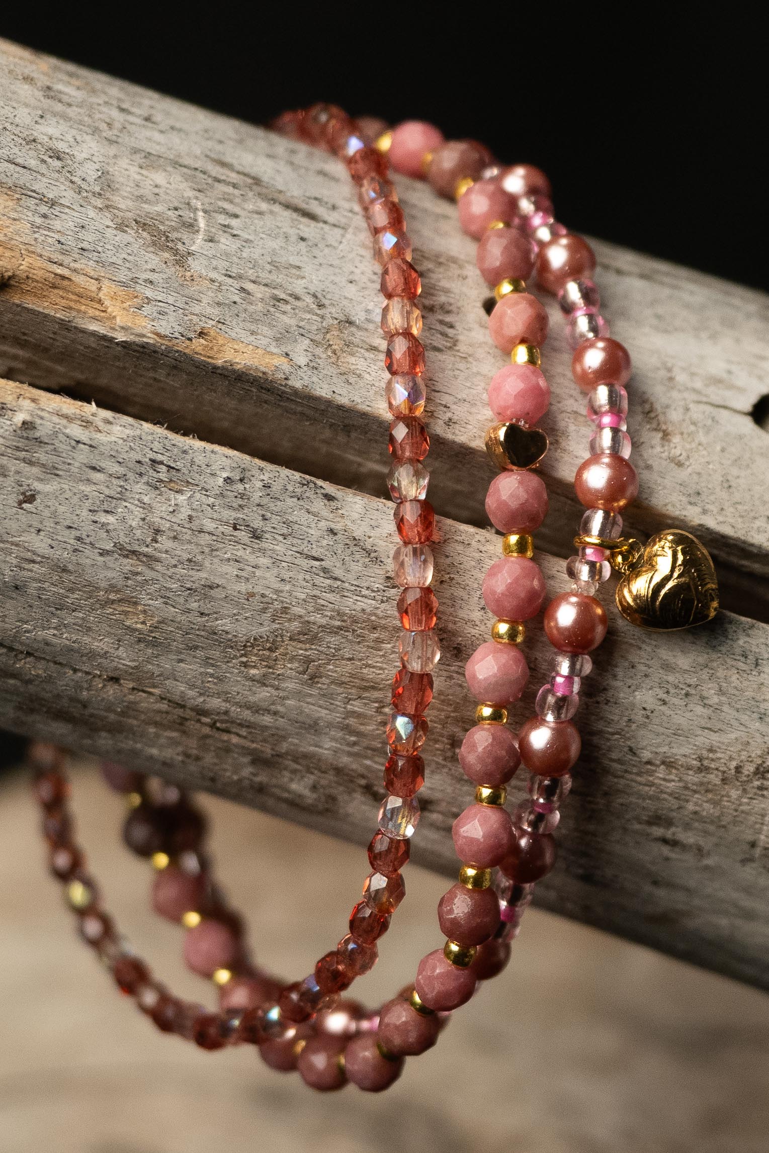 Three pink, clear, and purple beaded bracelets with a small heart-shaped charm on a wooden surface