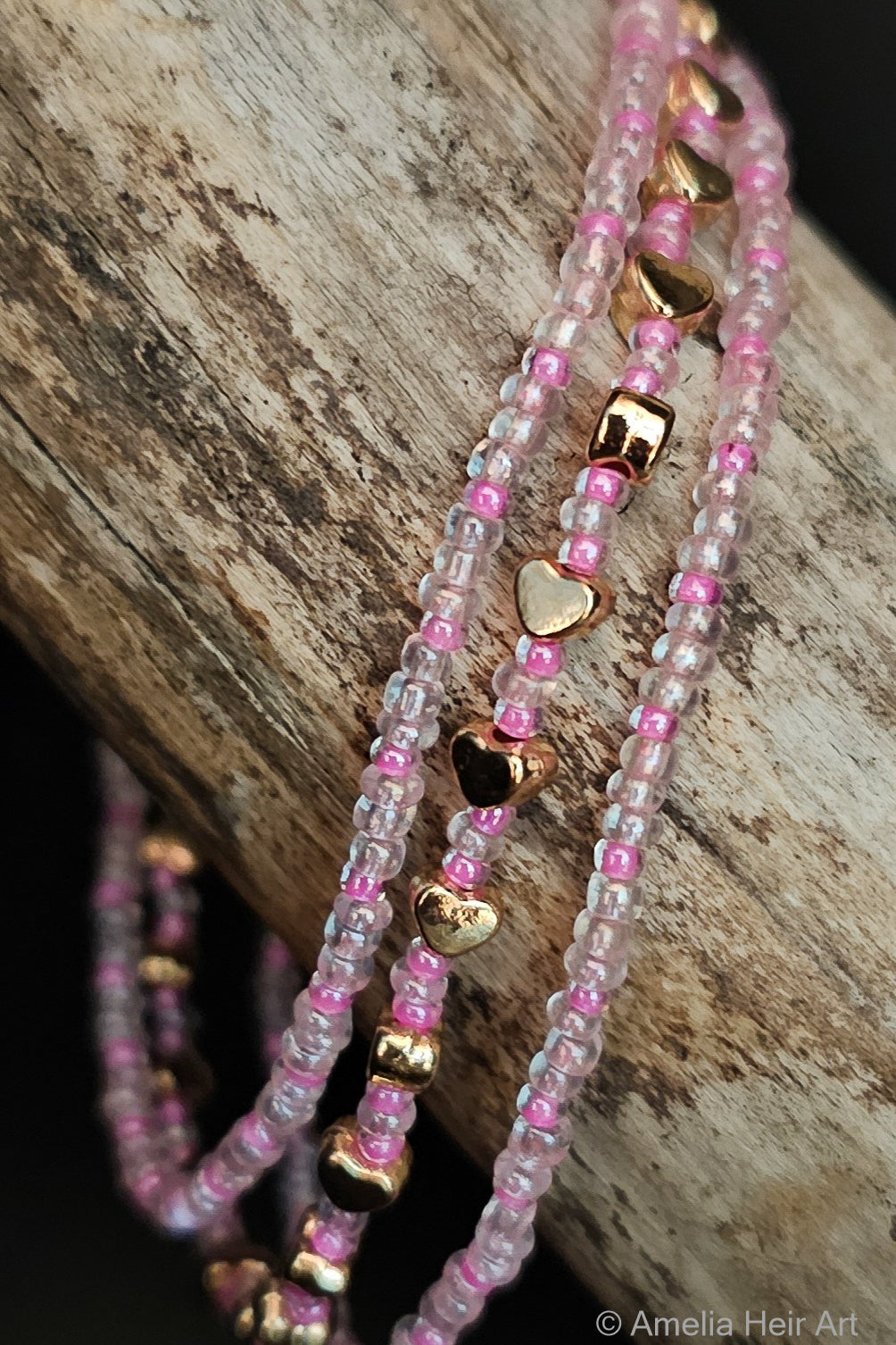 Three beaded bracelets with pink, clear, and gold accents on a wooden surface.