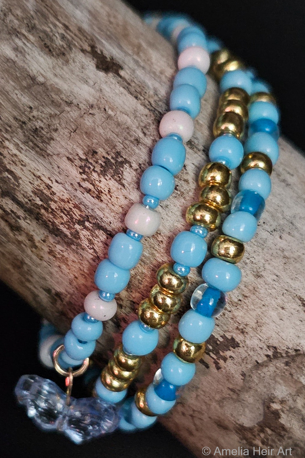 Three beaded bracelets with blue, gold, and white beads with a butterfly-shaped charm on a wooden surface.