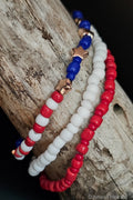 Three beaded bracelets in red, white, and blue on a wooden surface.