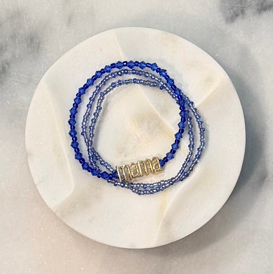 Three strand blue beaded crystal and glass stretch bracelet set with a gold 'mama' metal statement bead on a stone marble surface — Amelia Heir Art