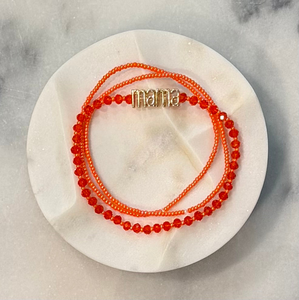 Three strand orange beaded crystal and glass stretch bracelet set with a gold 'mama' metal statement bead on a stone marble surface — Amelia Heir Art