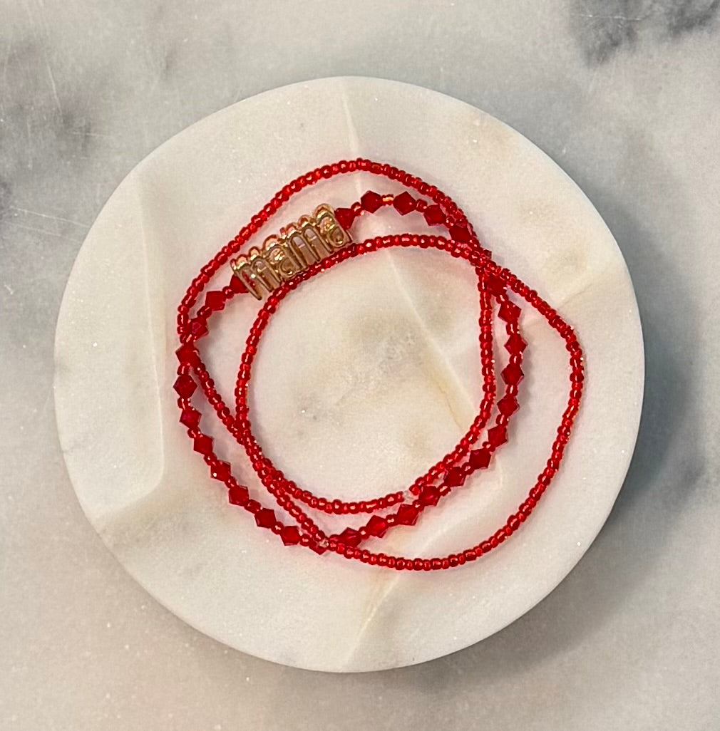 Three strand red beaded crystal and glass stretch bracelet set with a gold 'mama' metal statement bead on a stone marble surface — Amelia Heir Art