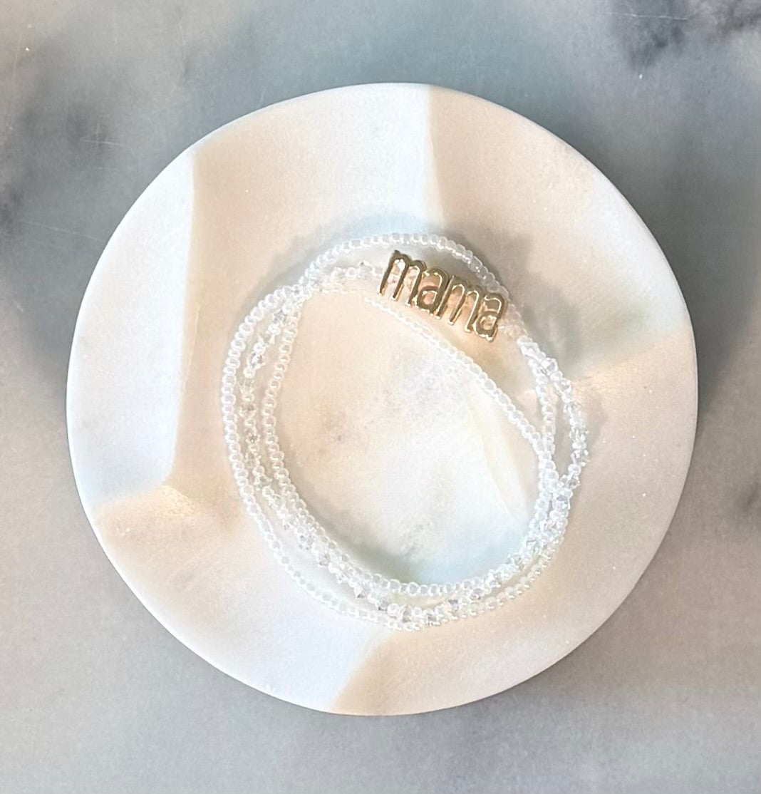 Three strand white beaded crystal and glass stretch bracelet set with a gold 'mama' metal statement bead on a stone marble surface — Amelia Heir Art