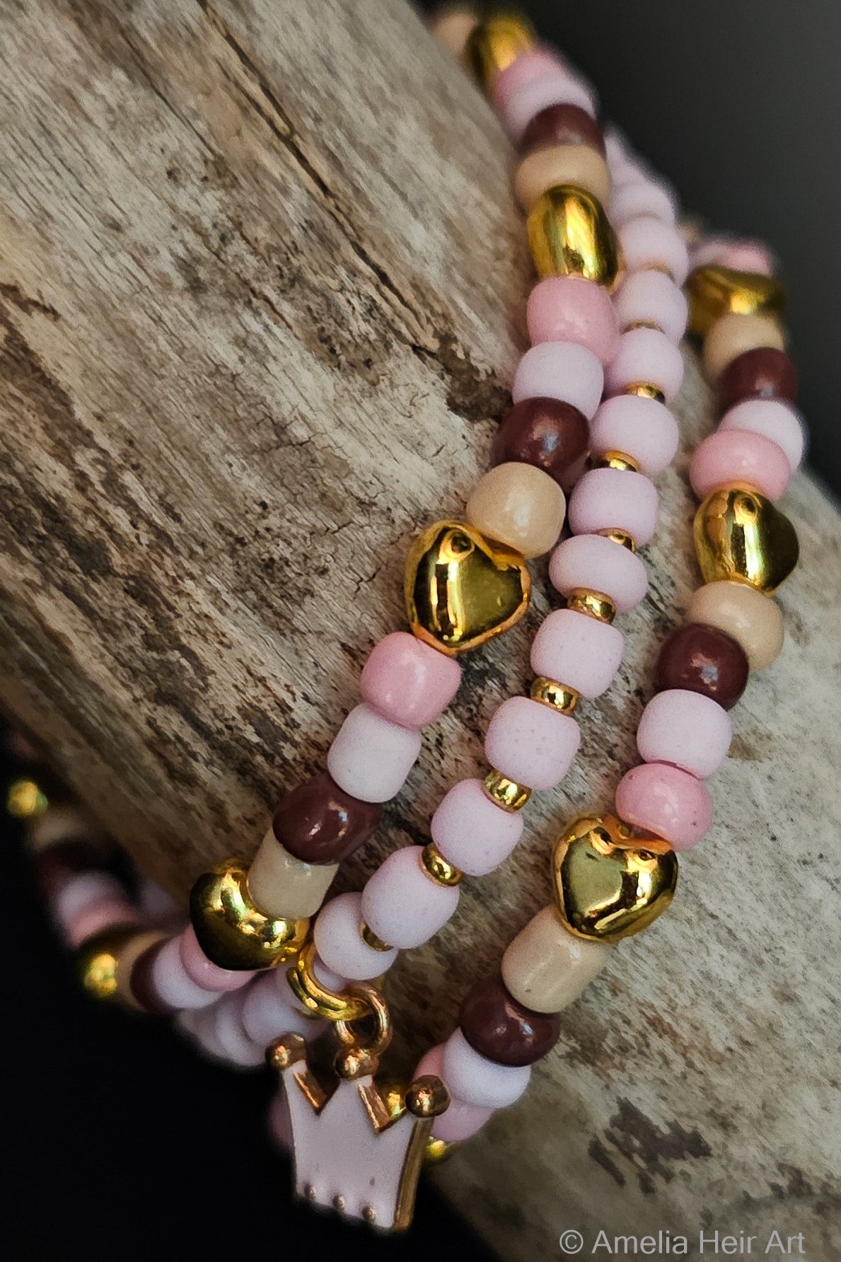 Stack of beaded bracelets with gold heart accents and a crown-shaped charm on a wooden surface