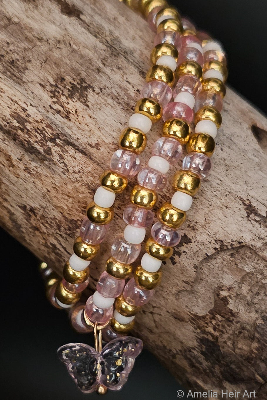 Beaded bracelet with gold, pink, and white beads with a butterfly-shaped charm on a wooden surface