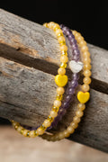 Three yellow and purple beaded bracelets with white hearts on a wooden surface