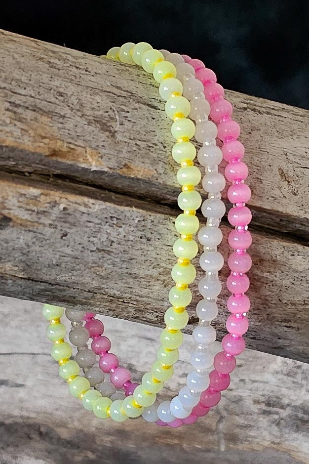 Three beaded bracelets in pink, yellow, and white on a wooden surface