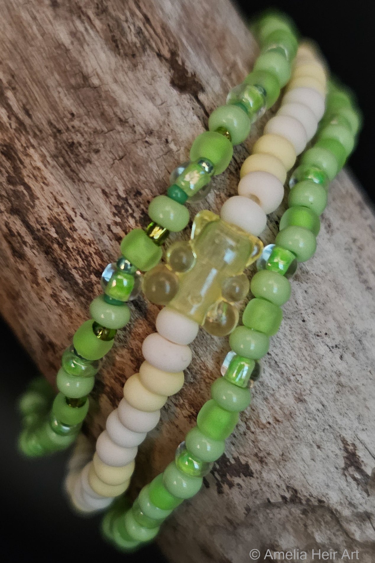 Three green and yellow beaded bracelets with a gummy-bear- shaped bead on a wooden surface