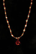 Necklace with red, green, and white beads with gift bow pendent on a black background
