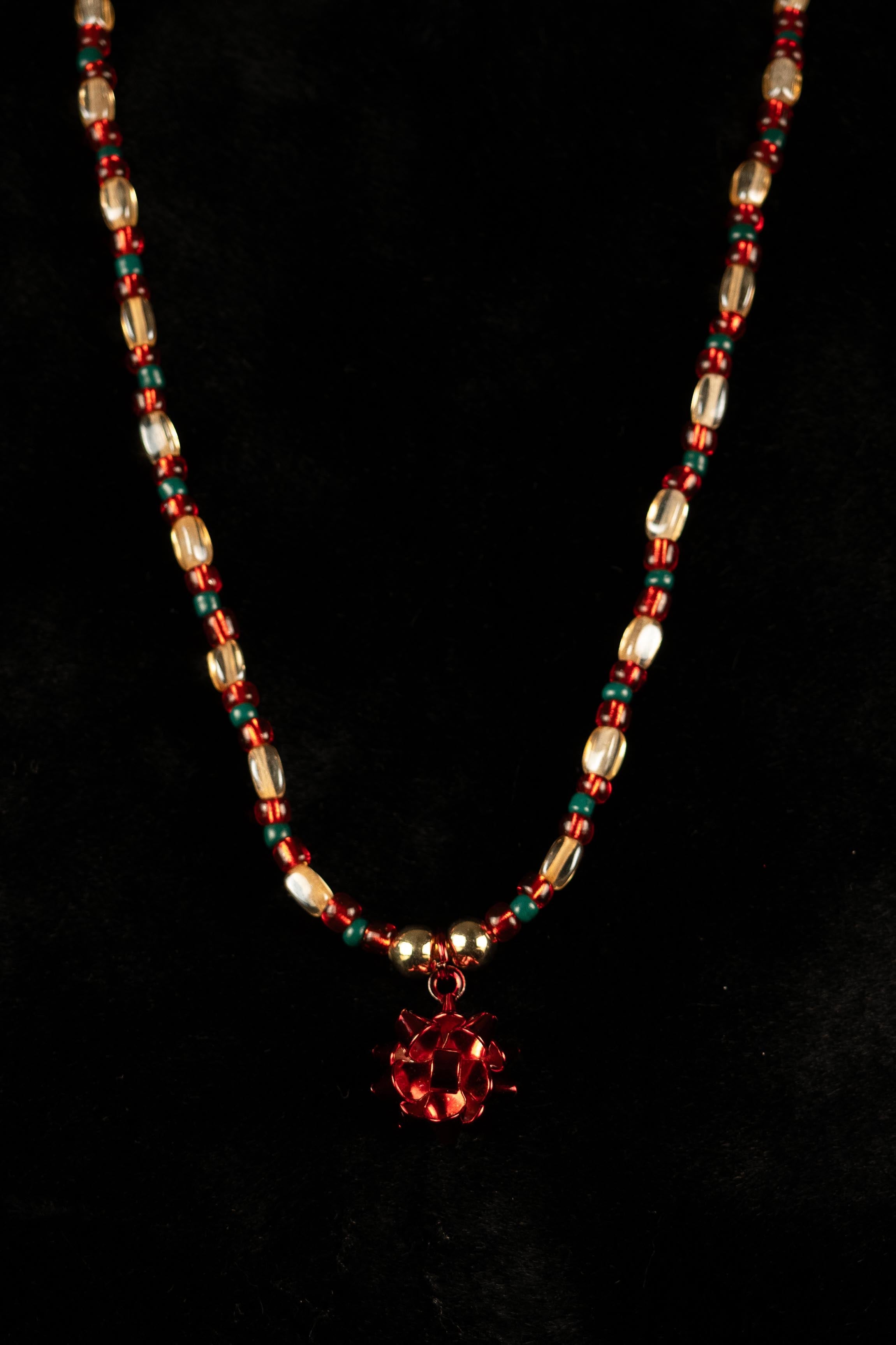 Necklace with red, green, and white beads with gift bow pendent on a black background