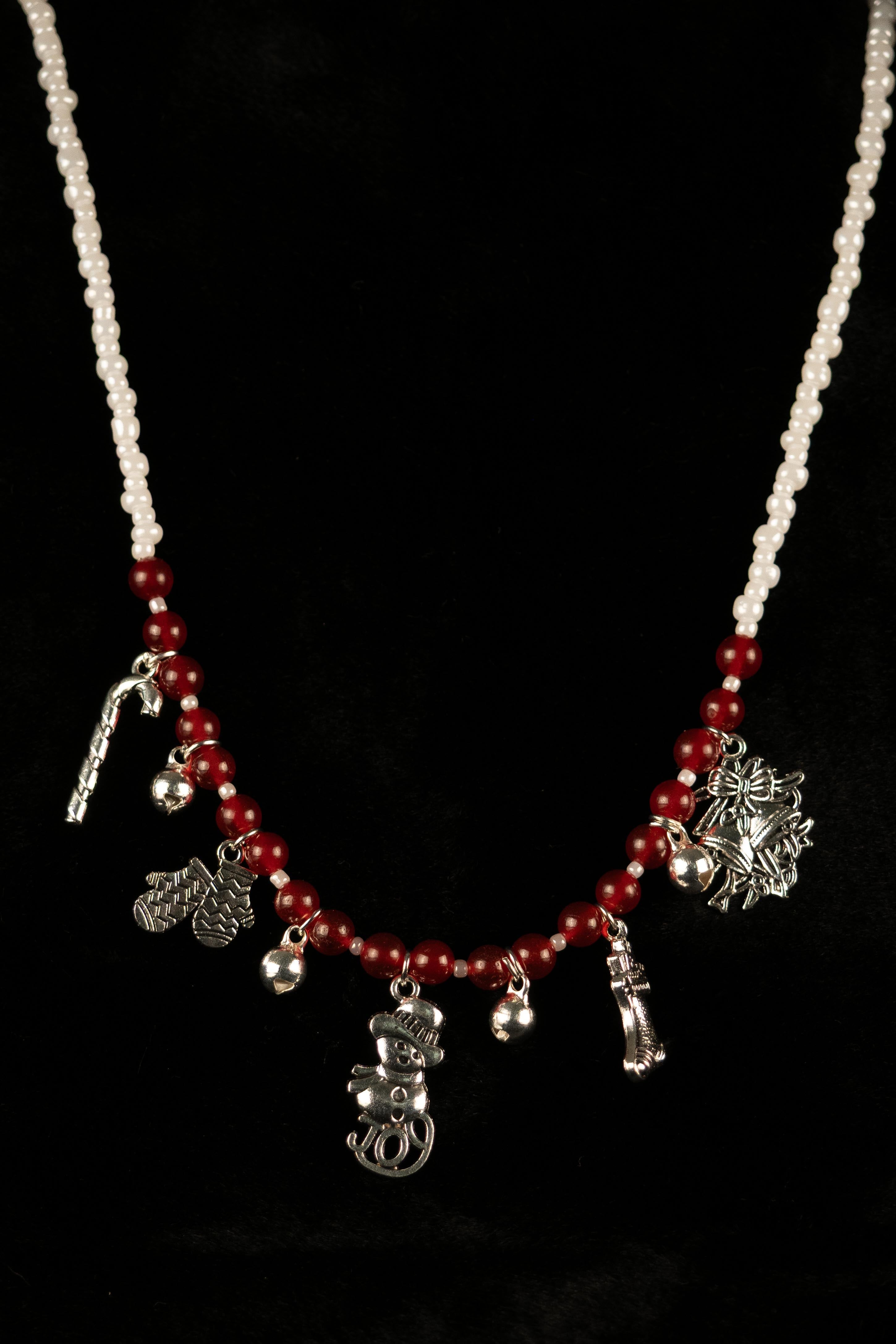 Necklace with red and white beads and silver holiday charms on a black background