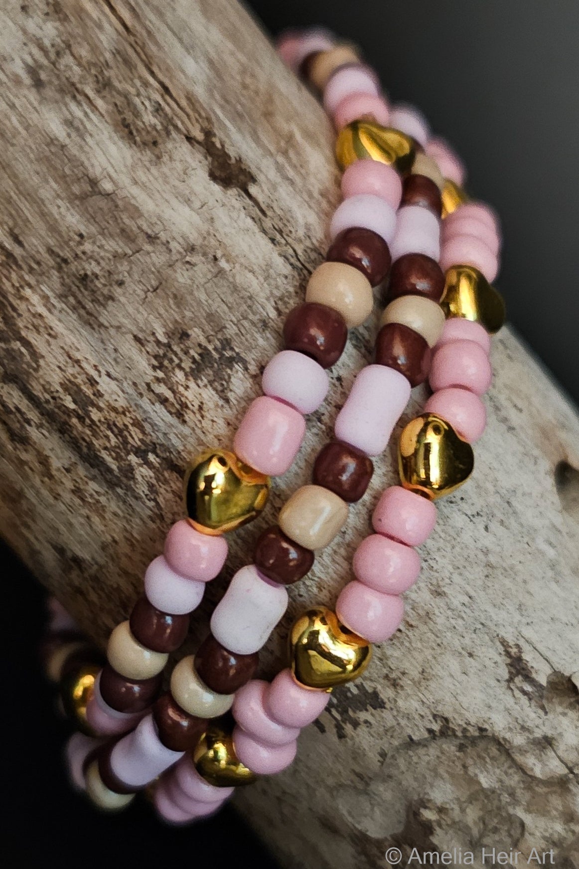Stack of pink, brown, and tan beaded bracelets with gold color heart-shaped beads on a wooden surface