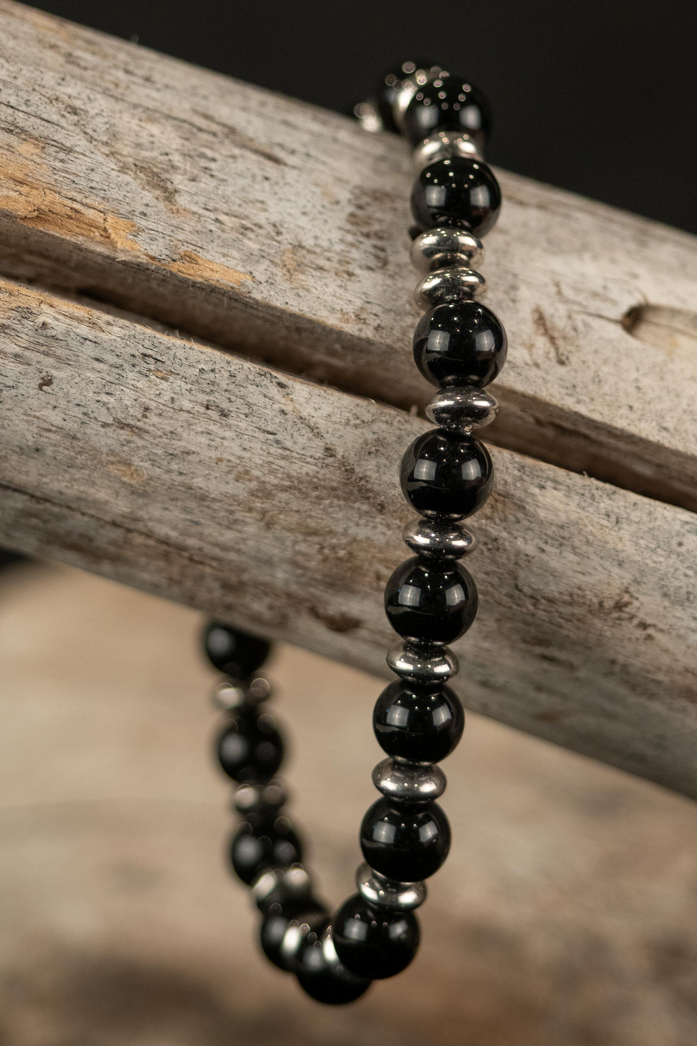 Black beaded bracelet with silver accents on a wooden surface