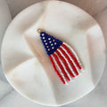 Handmade beaded American flag wind sock zipper pull with a woven blue star field and flowing red and white fringe strands, displayed on a white marble surface — One Nation Zipper Pull by Amelia Heir Art Designs