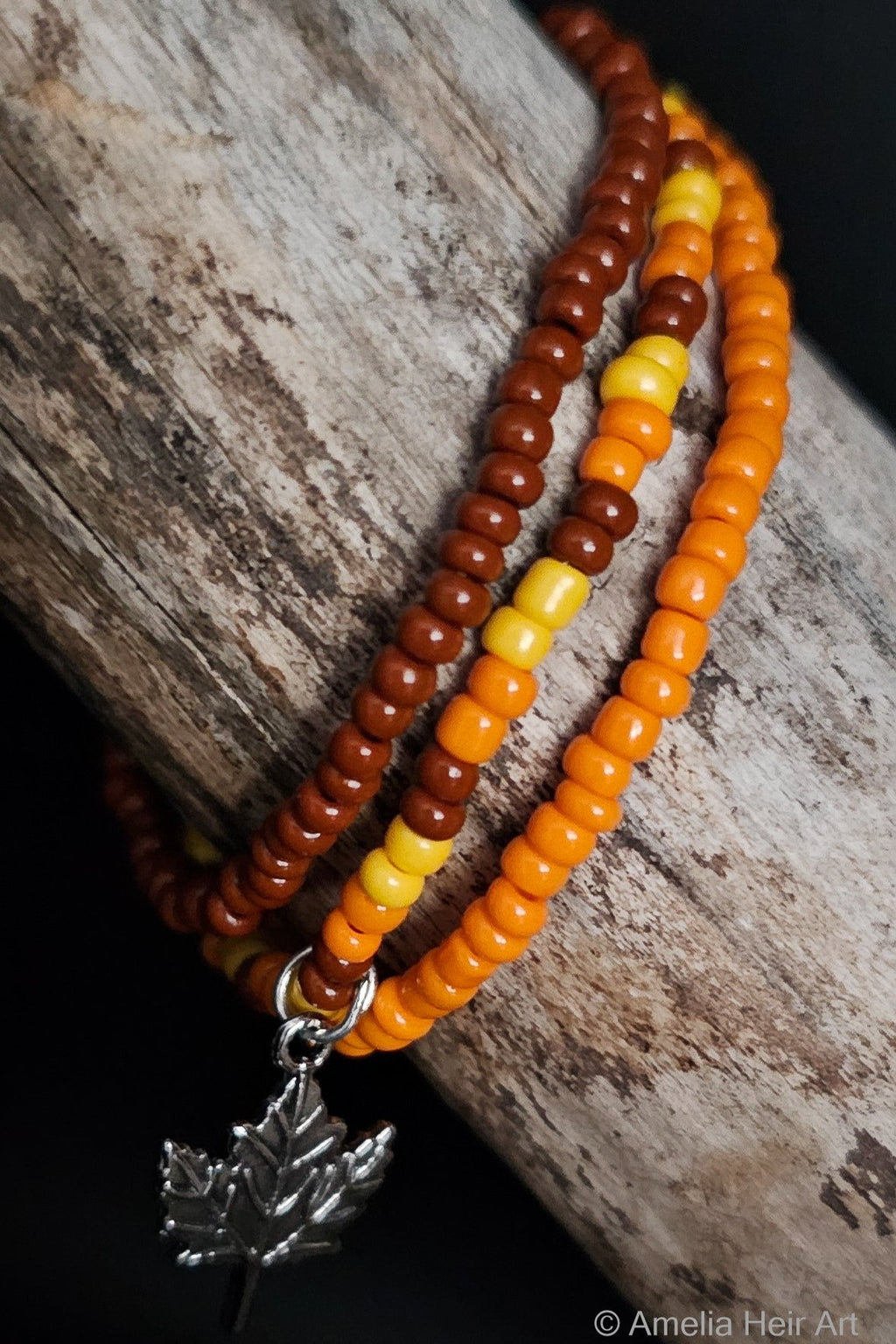 Pam handcrafted yellow orange silver and brown beaded bracelet set with leaf charm on a wooden surface — Amelia Heir Art