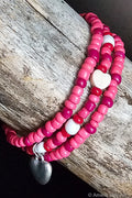 Stack of pink beaded bracelets with heart charms on a wooden surface