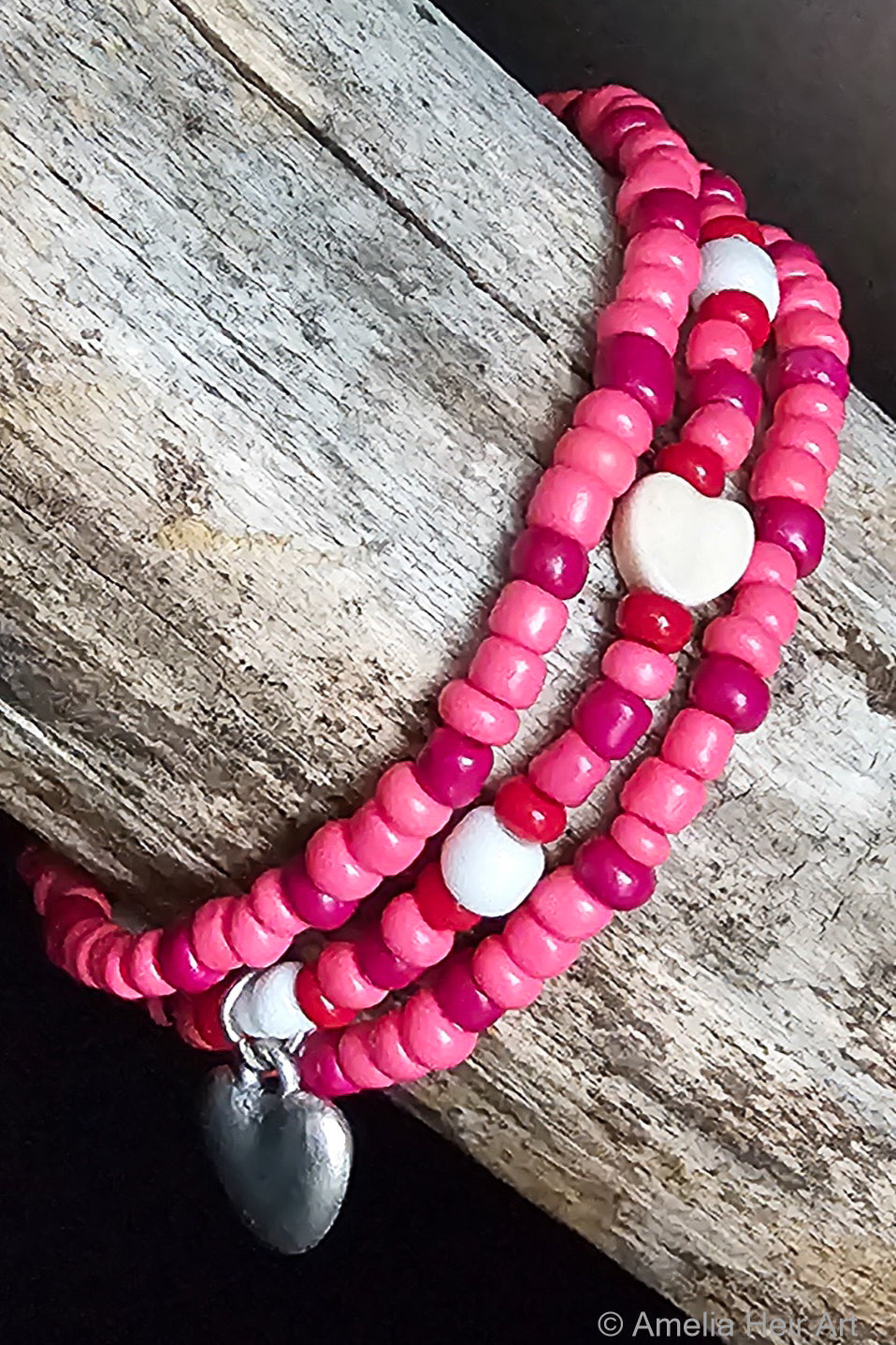 Stack of pink beaded bracelets with heart charms on a wooden surface