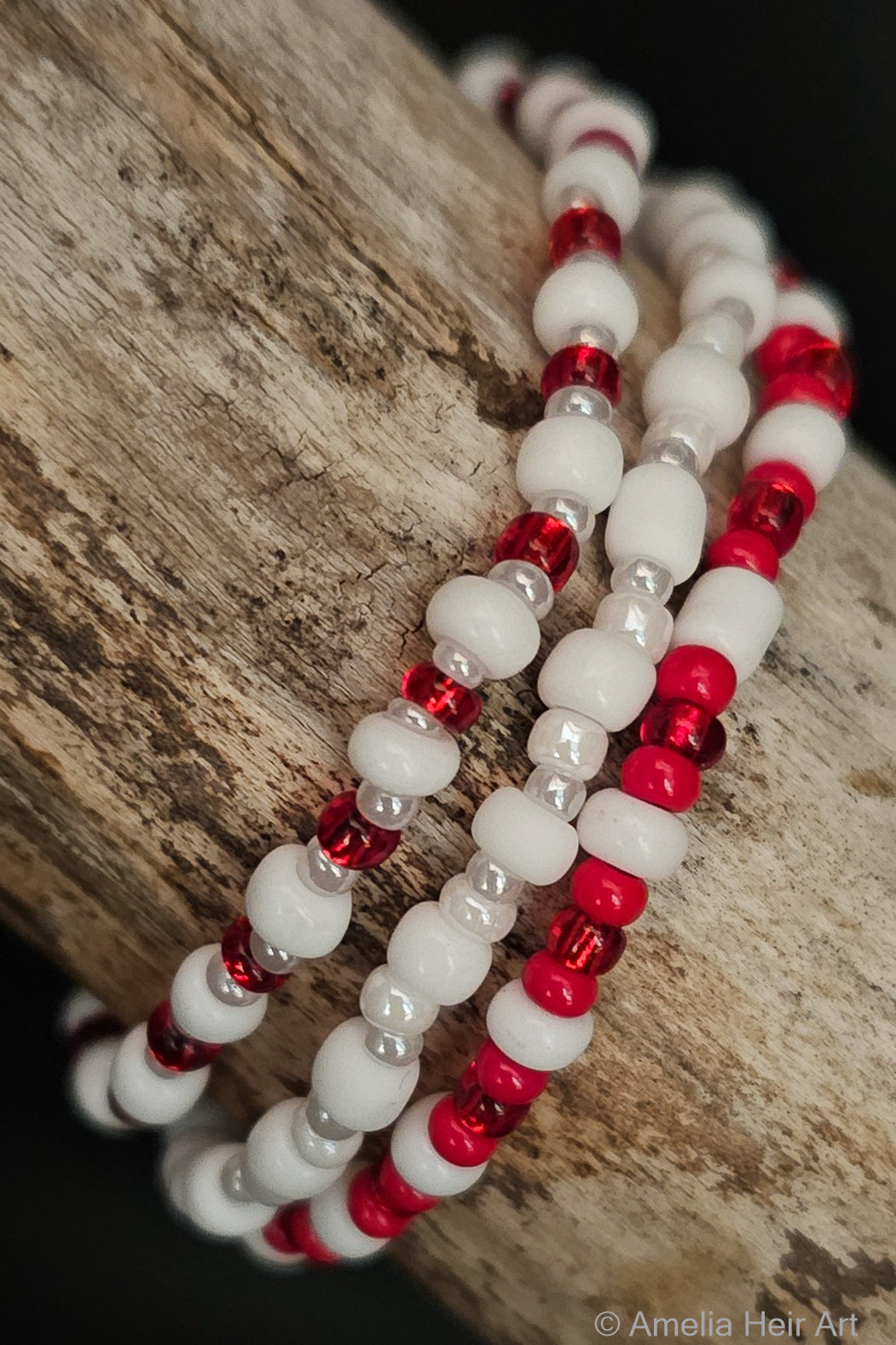 Three beaded bracelets with red and white beads on a wooden surface.