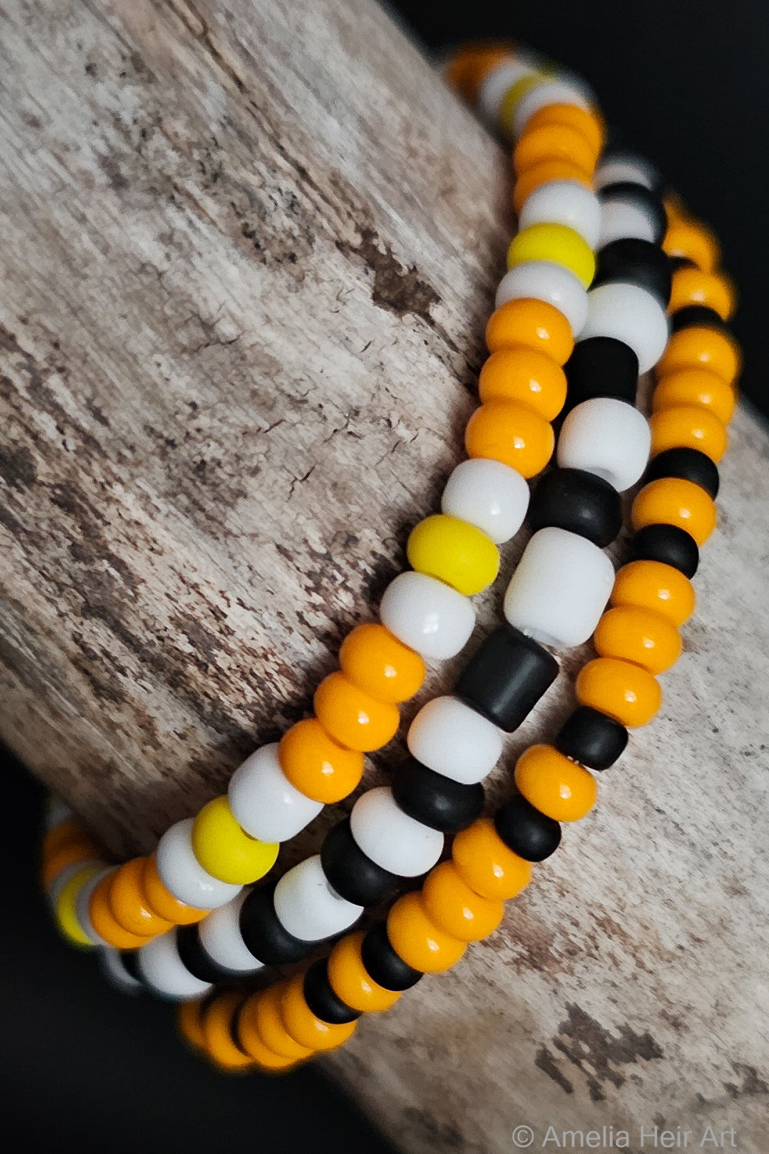Three beaded bracelets in orange, black, and white on a wooden surface