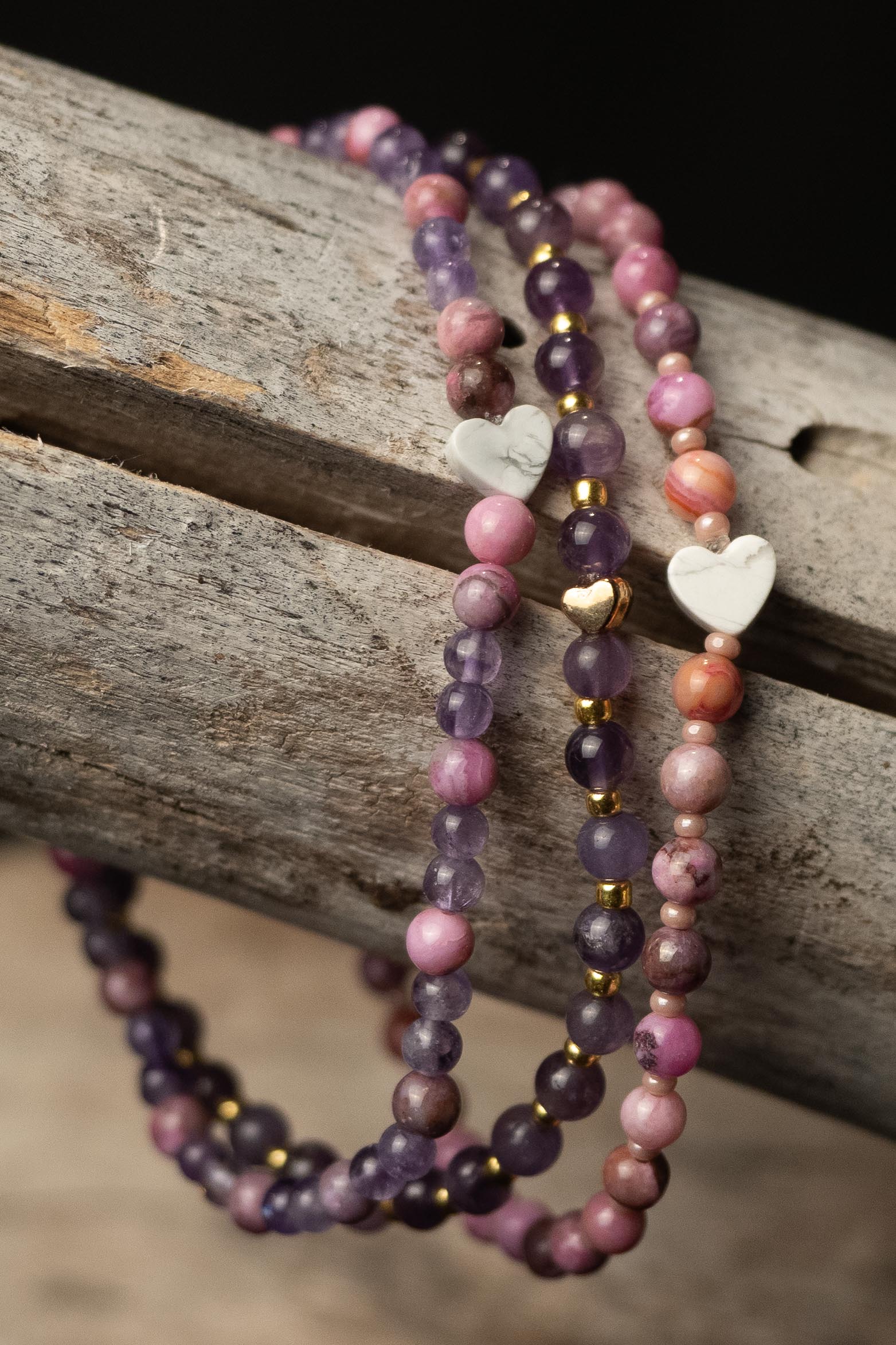 Pink and purple beaded bracelets with heart-shaped charms on a wooden surface