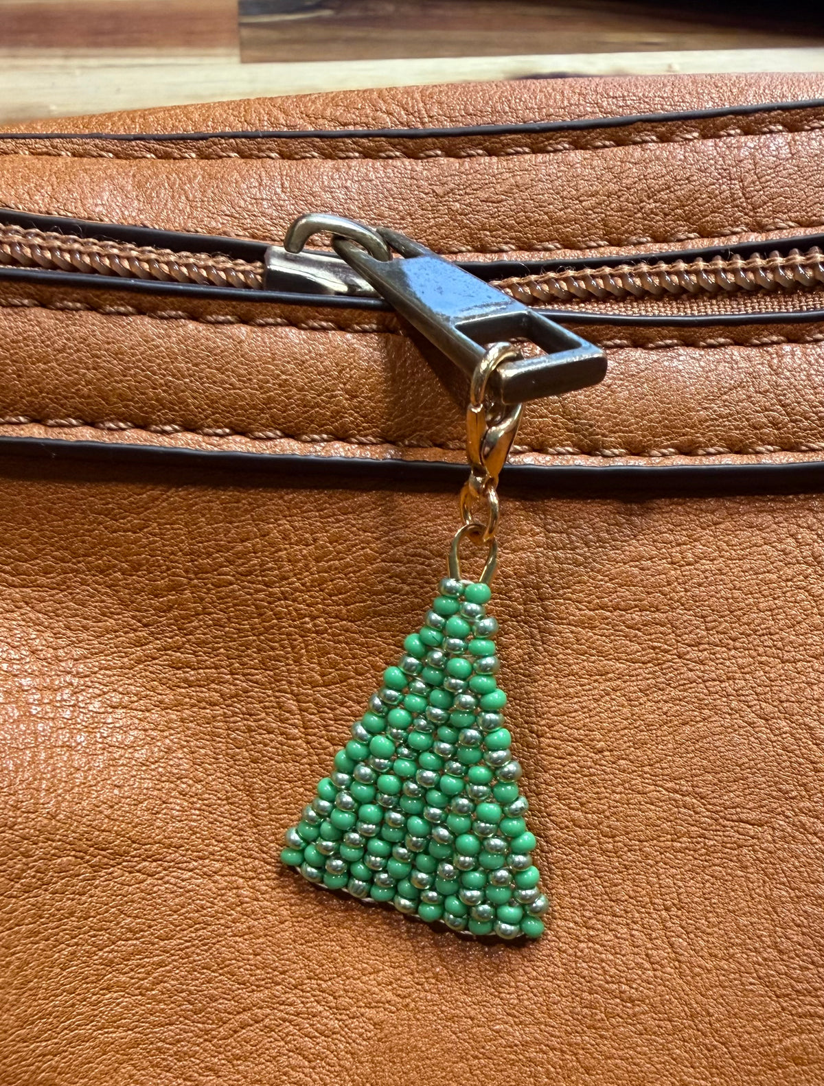 Christmas Pine handmade zipper pull by Amelia Heir Art, featuring green and metallic green beads in a pine tree shape attached to a brown leather bag’s zipper.