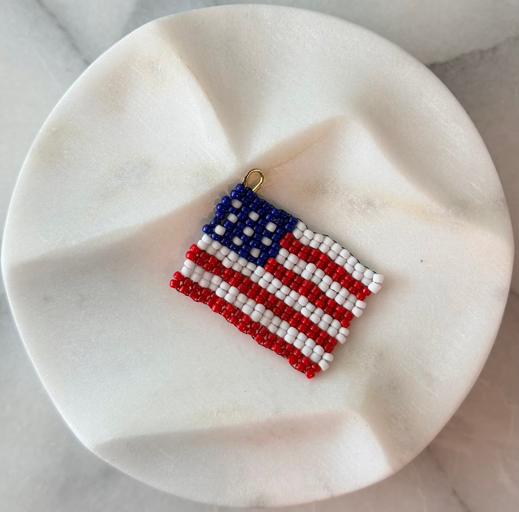 Handmade beaded American flag zipper pull in red, white, and blue seed beads with a gold loop, and lobster clasp displayed on a white marble surface — Pledge Zipper Pull by Amelia Heir Art Designs 