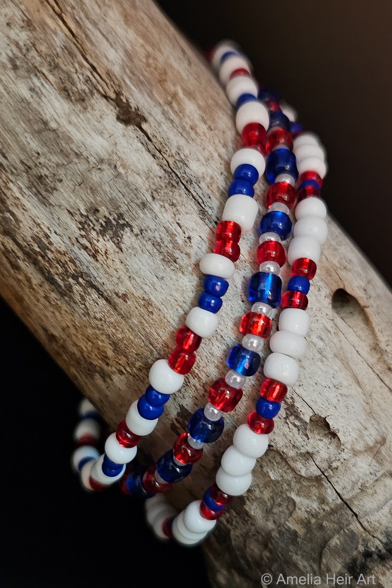 Three beaded bracelets in red, white, and blue on a wooden surface.