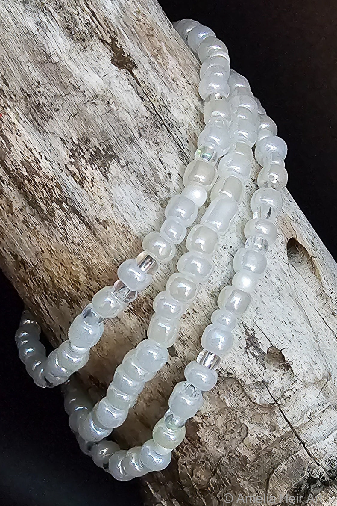 Three white beaded bracelets on a wooden surface