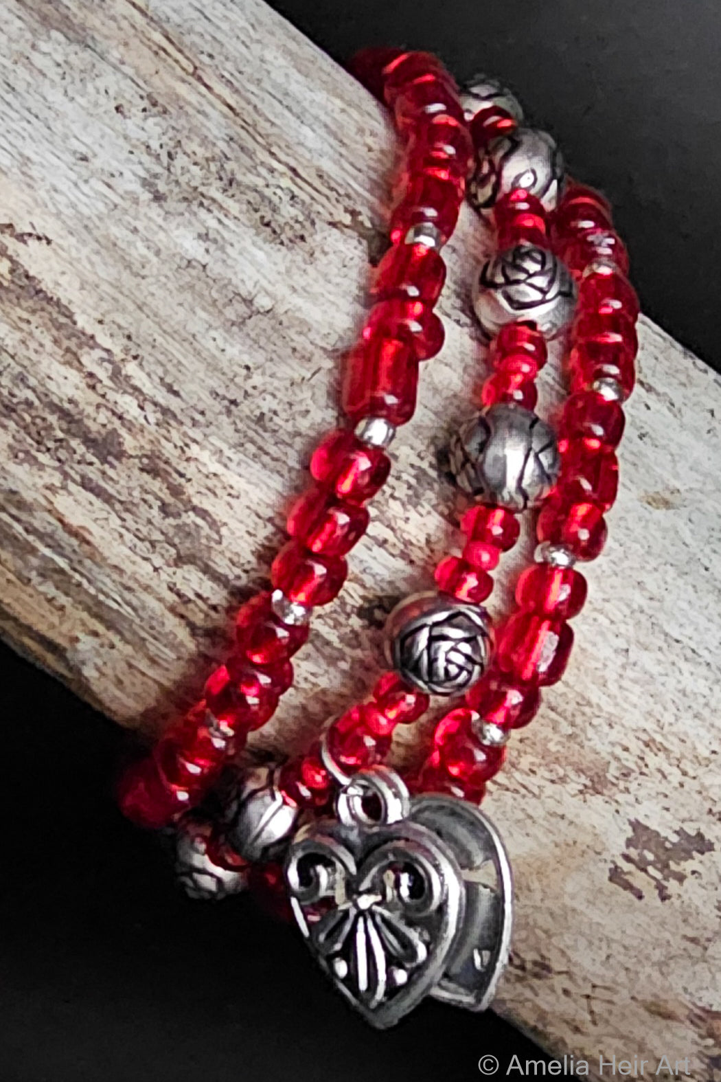 Red beaded bracelet with silver heart charm and silver rose-shaped beads on a wooden surface