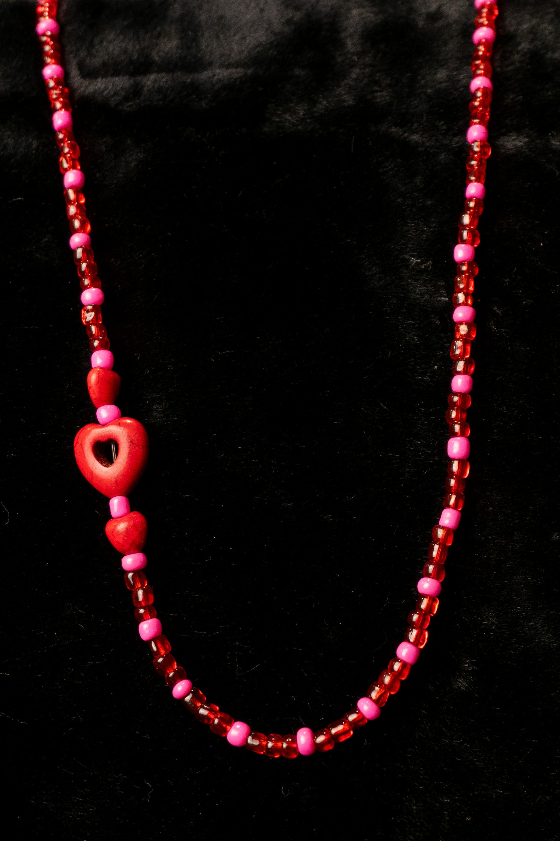 Necklace with red and pink beads and heart-shaped charm on a black background