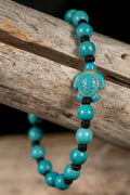 Turquoise colored beaded bracelet with a turtle charm on a wooden surface