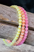 Set of three beaded bracelets in pink, yellow, and orange on a wooden surface