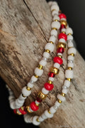 Three beaded bracelets with white, red, and gold beads on a wooden surface.
