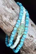 Set of blue and green beaded bracelets with a gummy bear bead on a wooden surface