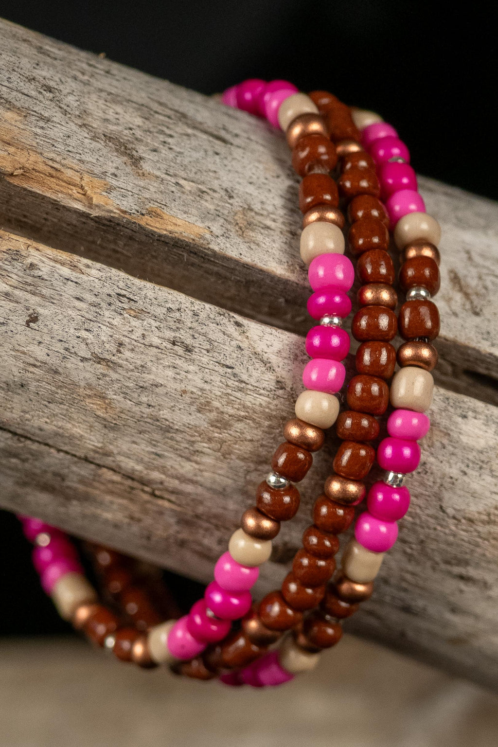 Stack of beaded bracelets in pink, brown, and beige on a wooden surface