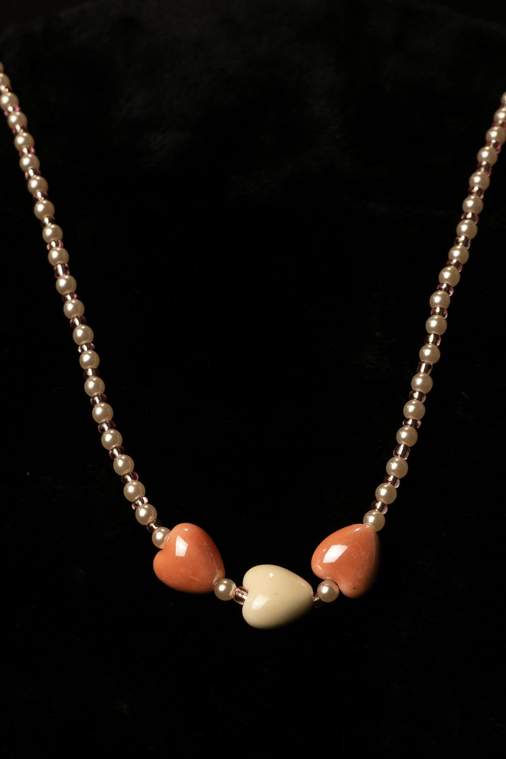 Snuggly handcrafted white and brown beaded necklace with heart charm on a black background — Amelia Heir Art